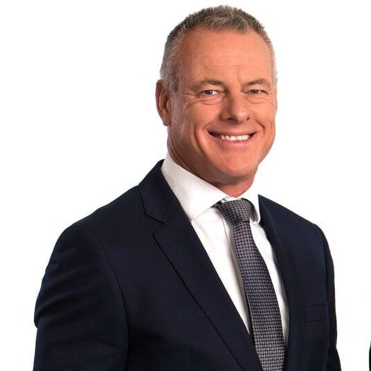 Two smiling men in navy suits and gray ties stand side by side against a white background, presenting a professional image.